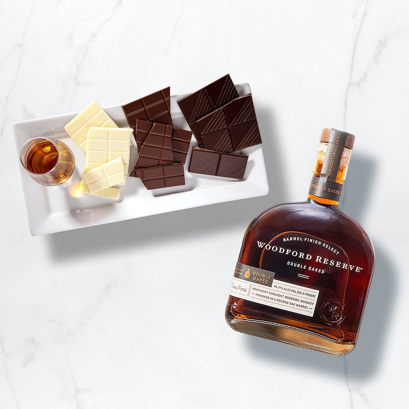 Load image into Gallery viewer, Woodford Reserve double oak 
bourbon bottle with chocolate bars and a small bowl on a white marble surface