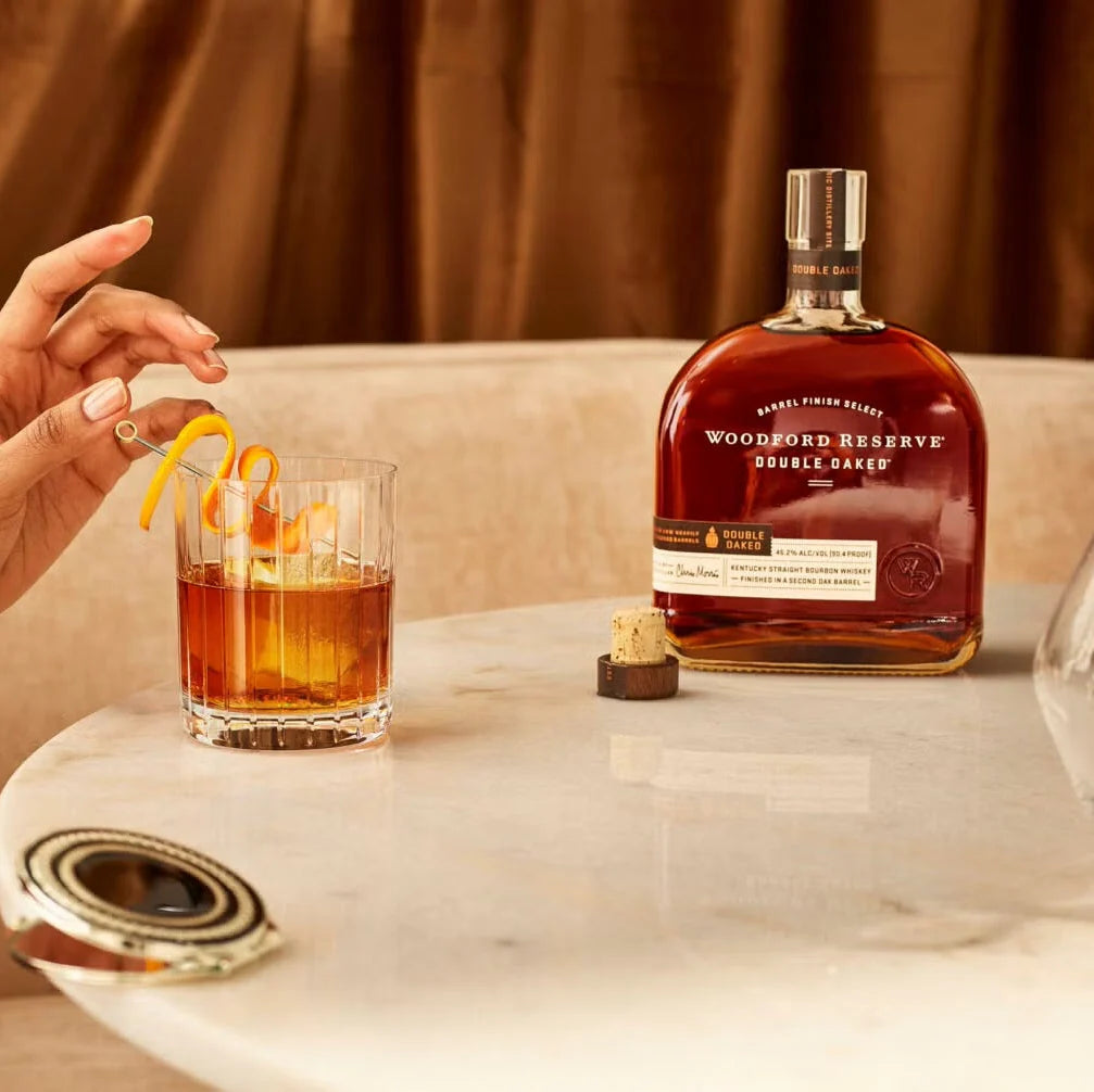Load image into Gallery viewer, A bottle of an open bourbon and a cocktail on a marble table.