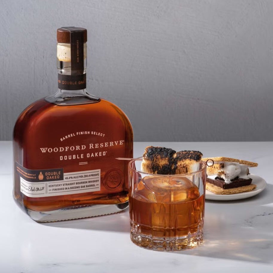 Woodford Reserve Double Oaked bourbon bottle with a glass of whiskey on a white surface.
