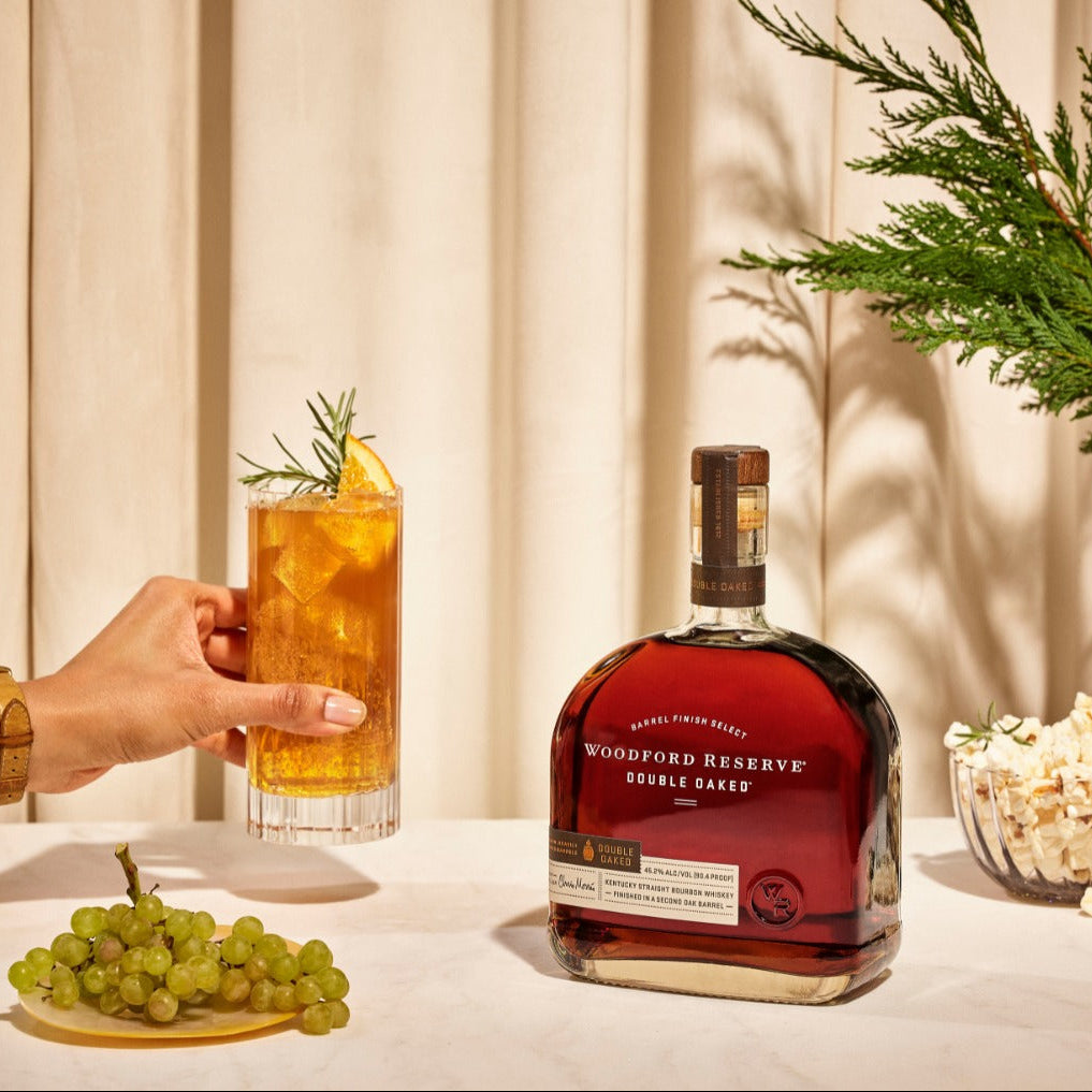 Load image into Gallery viewer, Woodford Reserve double oak bourbon bottle with a cocktail and snacks on a table