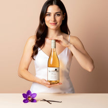 Load image into Gallery viewer, Woman holding a bottle of Wooing Tree Blondie Rose wine with a purple flower and vanilla bean on a beige background