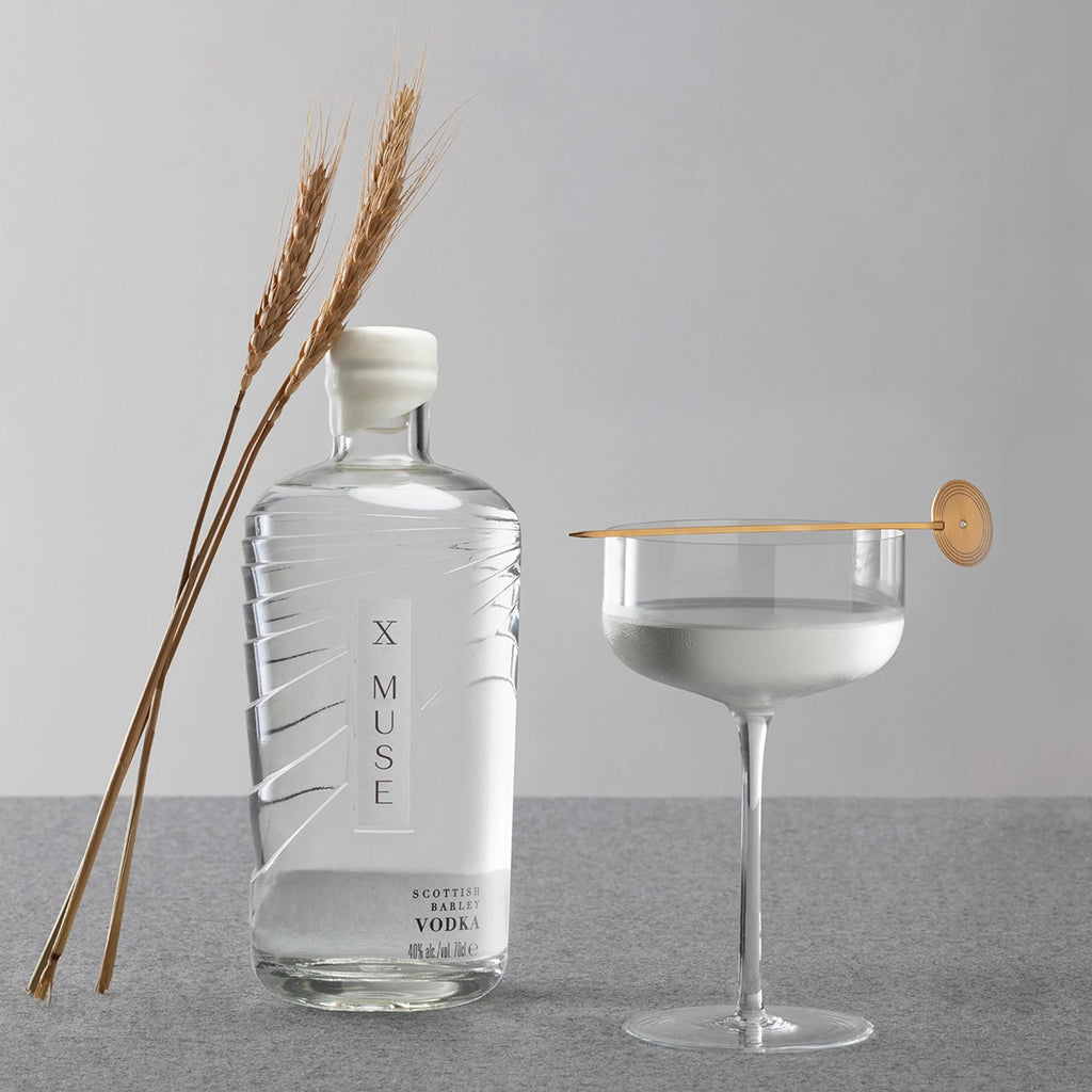 X Muse vodka bottle with a glass of vodka and a cocktail stick on a gray surface.