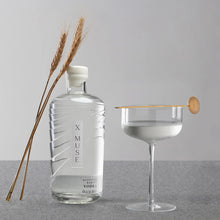 Load image into Gallery viewer, X Muse vodka bottle with a glass of vodka and a cocktail stick on a gray surface.