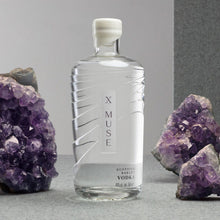 Load image into Gallery viewer, X Muse vodka bottle with amethyst crystals on a gray background