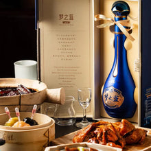 Load image into Gallery viewer, Blue bottle with a ribbon, accompanied by food items and a glass on a table.