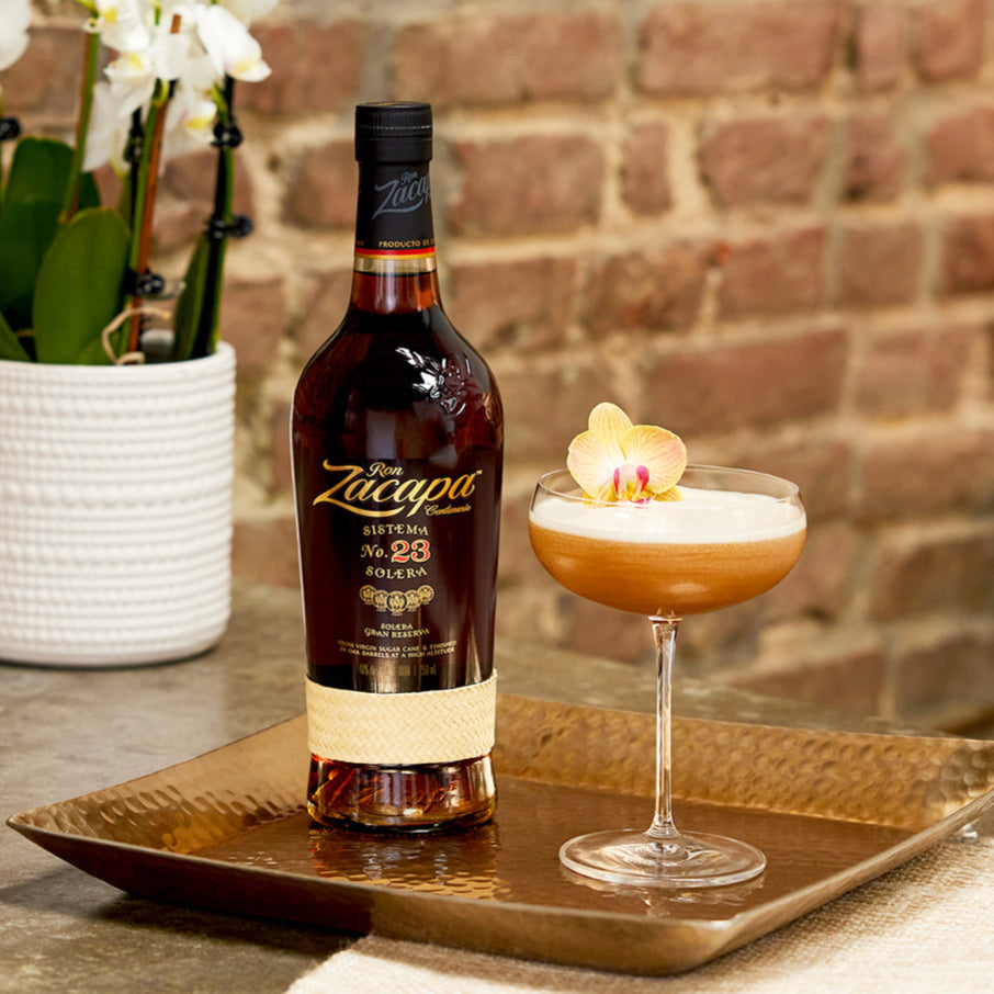 Load image into Gallery viewer, Zacapa 23 rum bottle with a cocktail on a tray against a brick wall.
