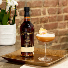 Load image into Gallery viewer, Zacapa 23 rum bottle with a cocktail on a tray against a brick wall.