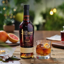 Load image into Gallery viewer, Bottle of Ron Zacapa 23 aged rum on a table with a glass of cocktail and fruit.