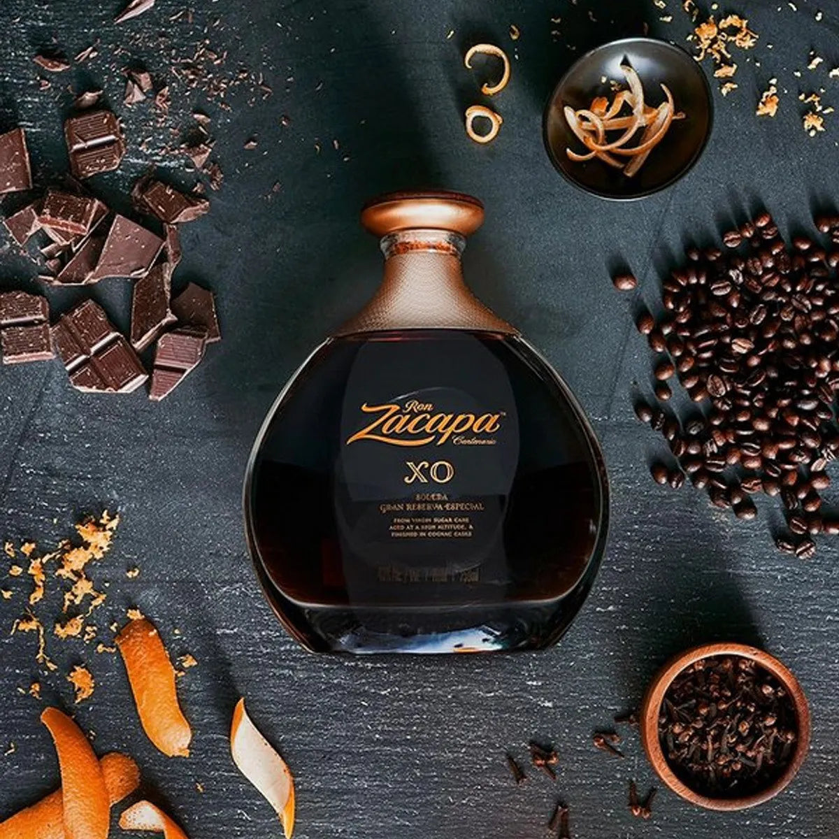 Load image into Gallery viewer, Bottle of Ron Zacapa XO rum surrounded by chocolate pieces, coffee beans, and spices on a dark surface.