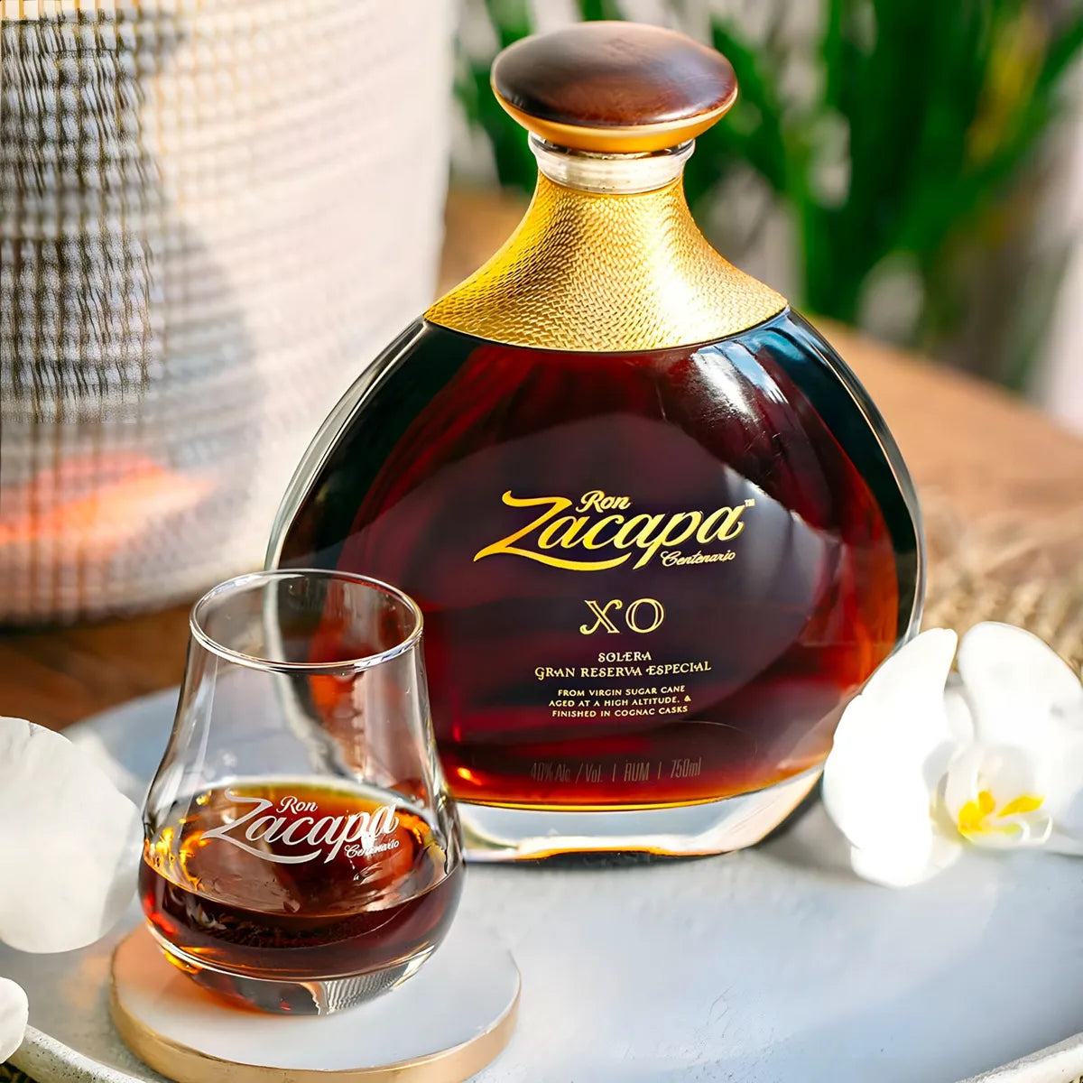 Load image into Gallery viewer, Ron Zacapa XO rum bottle with a glass of rum on a table with flowers and decor.