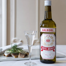 Load image into Gallery viewer, Bottle of Taffel Akvavit with a glass on a table with food in the background