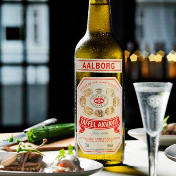 A bottle of Aalborg Akvavit and a snaps on a table with some food 
