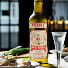 Load image into Gallery viewer, A bottle of Aalborg Akvavit and a snaps on a table with some food 