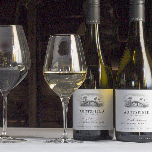 Wine bottles and glasses on a rustic wooden table with a barn-style background.