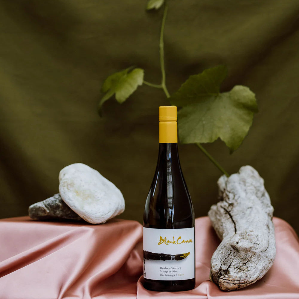 Wine bottle with yellow cap on a pink surface with rocks and greenery