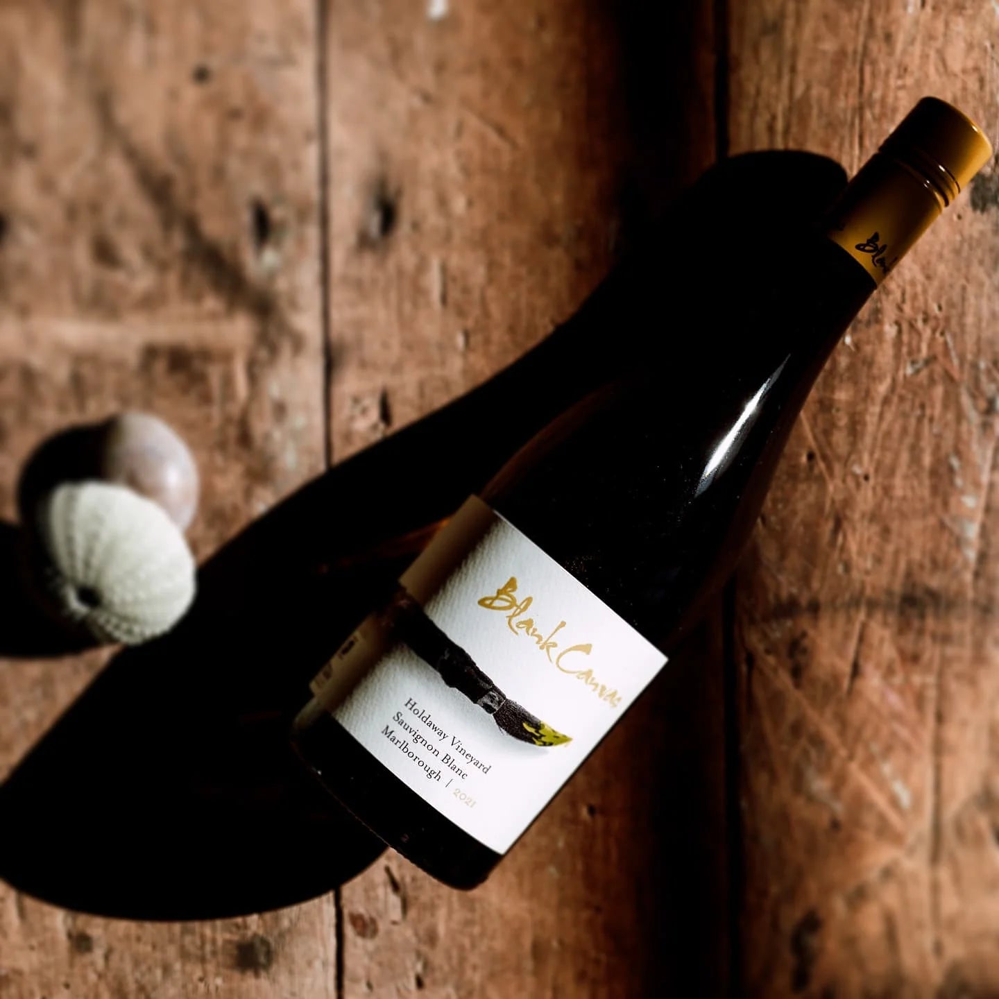 Load image into Gallery viewer, A bottle of white wine on a wooden surface and some shells.