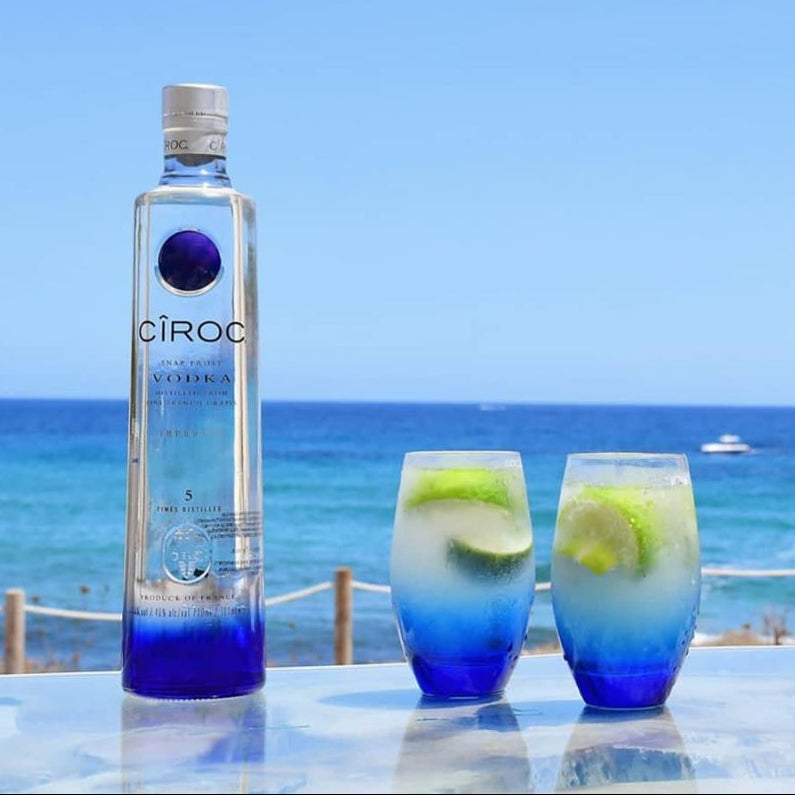 Load image into Gallery viewer, Ciroc vodka bottle with two blue-themed cocktails by the ocean