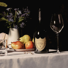 Load image into Gallery viewer, A bottle of Dom Perignon champagne on a table with a white table cloths and some flowers on it 