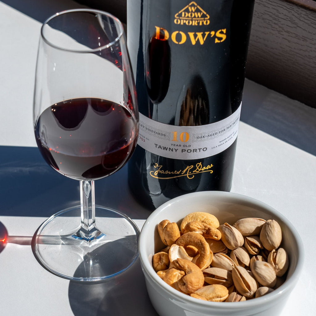 Bottle of Dow's Porto wine with a glass and bowl of nuts on a white surface