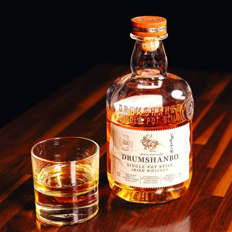 Load image into Gallery viewer, Bottle and glass of Drumshanbo whiskey on a wooden surface with a dark background