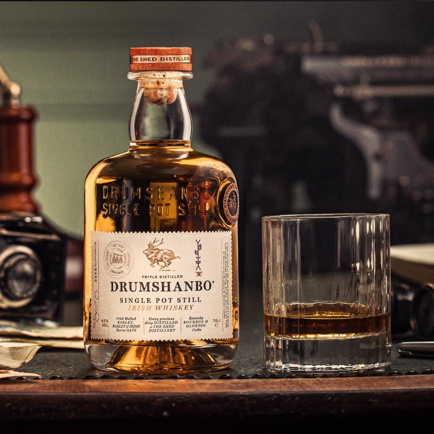 Load image into Gallery viewer, Drumshanbo single pot still Irish whiskey bottle with a glass on a wooden surface.