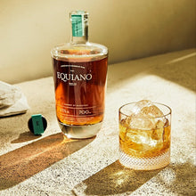 Load image into Gallery viewer, Bottle of Equiano rum and a glass with ice on a sandu wooden surface