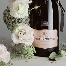 Load image into Gallery viewer, Champagne bottle with &#39;Fleur de Miraval&#39; label surrounded by flowers on a grey background