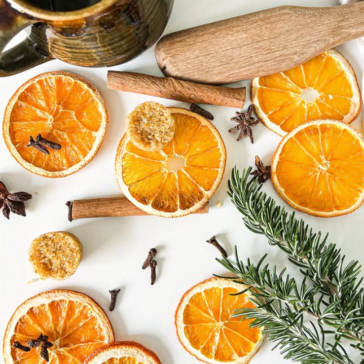 Load image into Gallery viewer, A styled flat-lay of FN Lemon dried orange slices, cinnamon sticks, star anise, cloves, a small piece of ginger, and a rosemary sprig arranged around a dark ceramic mug and a wooden rolling pin on a white surface.