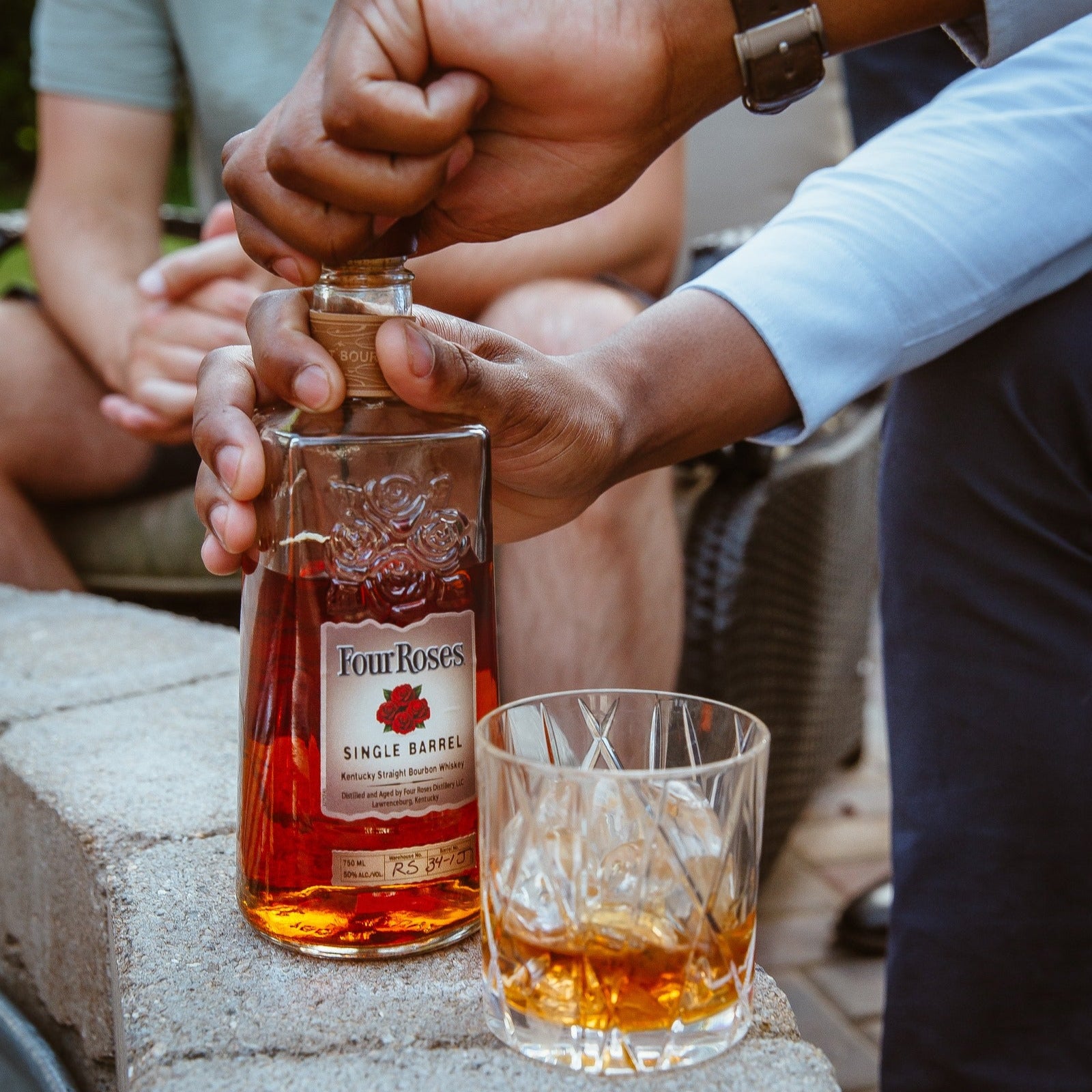 Load image into Gallery viewer, Person opening a bottle of Four Roses whiskey with a glass nearby.