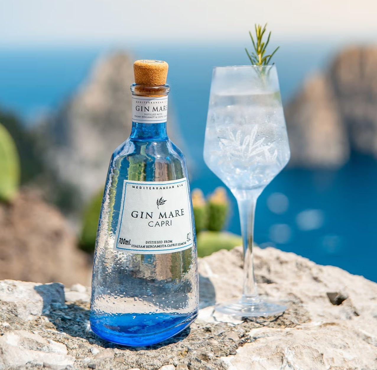 Load image into Gallery viewer, Gin Mare Capri bottle with a glass on a rocky surface with a blurred natural background