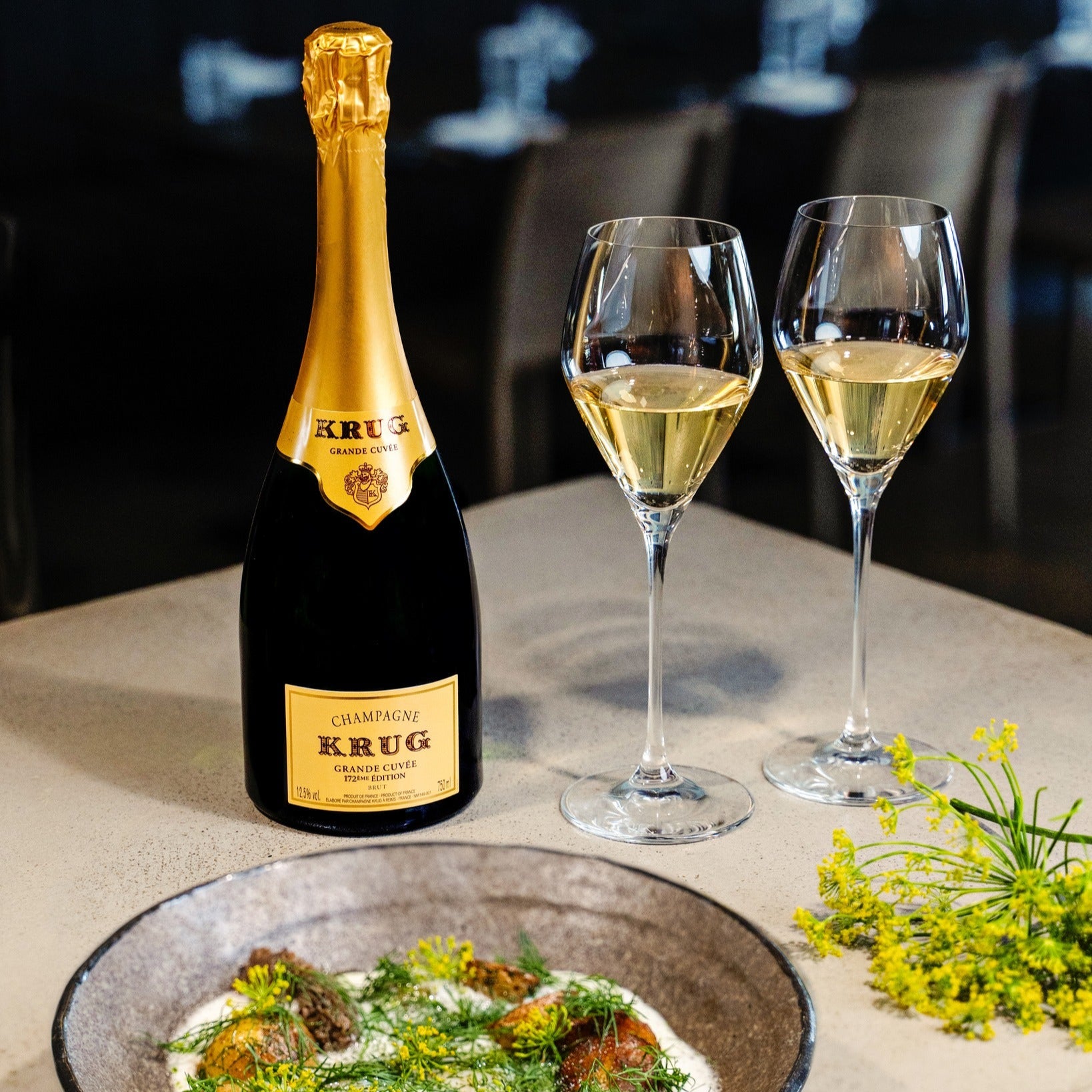 Load image into Gallery viewer, Bottle of Krug champagne with two glasses and a dish on a table.