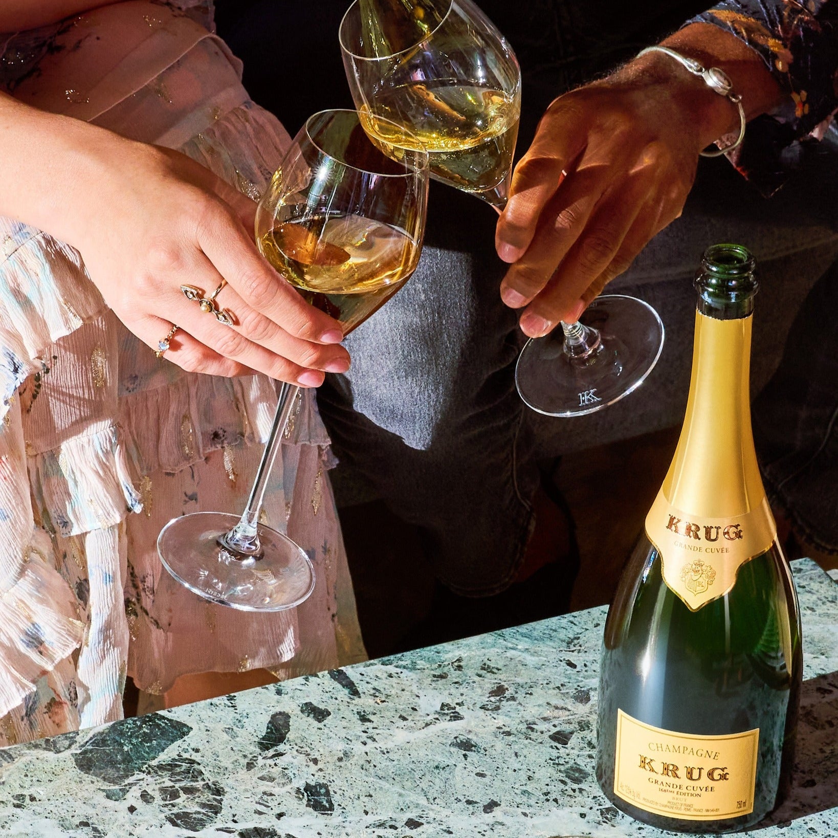 Load image into Gallery viewer, Two people clinking champagne glasses with a bottle of Krug champagne on a table.
