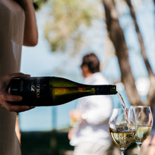 Load image into Gallery viewer, Person pouring wine from a bottle into glasses with a blurred outdoor background