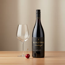 Load image into Gallery viewer, Bottle of Man O&#39; War Syrah wine with a glass and cherry on a wooden table