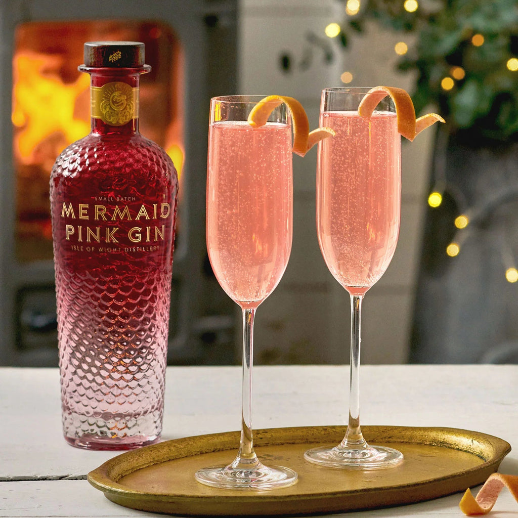 Mermaid Pink Gin bottle with two pink cocktails on a tray in front of a fireplace.