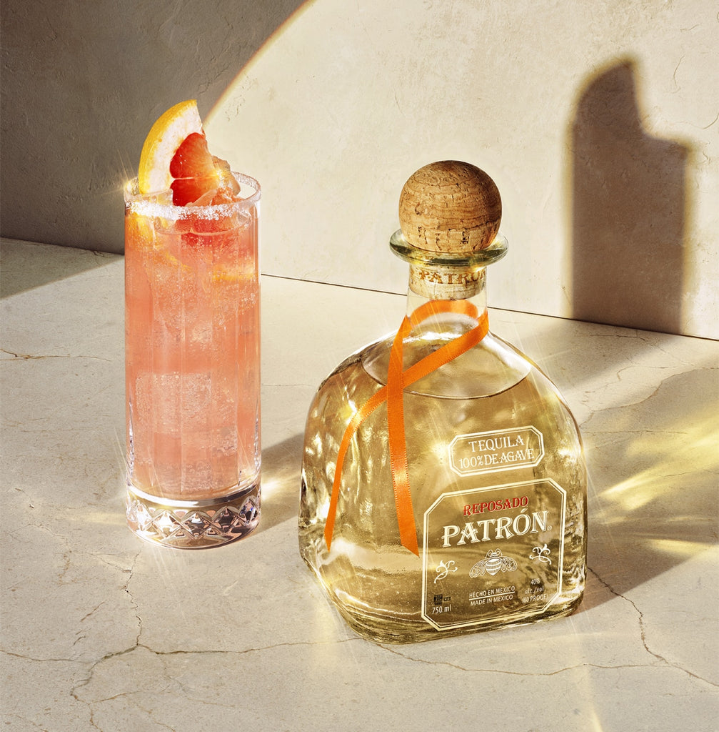 Patrón tequila bottle with a cocktail garnished with grapefruit on a light surface.
