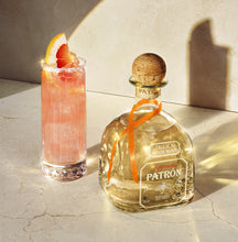 Load image into Gallery viewer, Patrón tequila bottle with a cocktail garnished with grapefruit on a light surface.