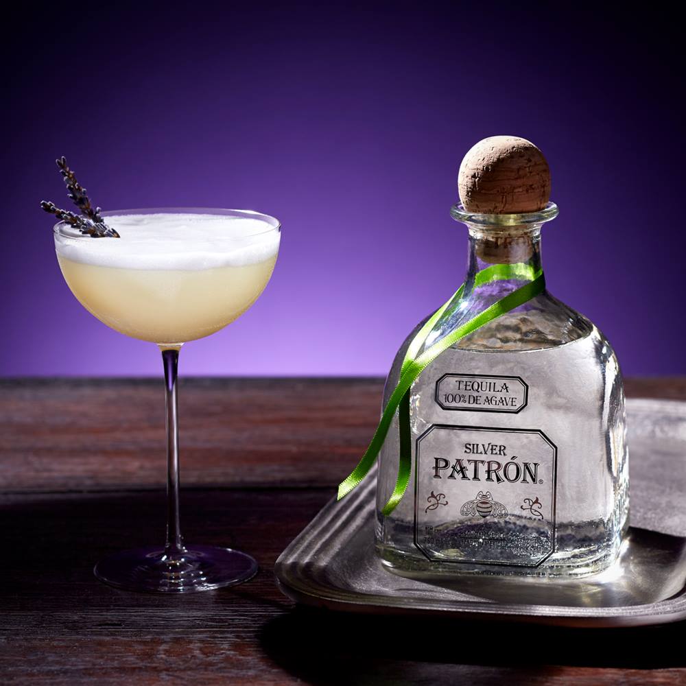 Load image into Gallery viewer, Silver Patron tequila bottle with a cocktail garnished with lavender on a wooden surface.