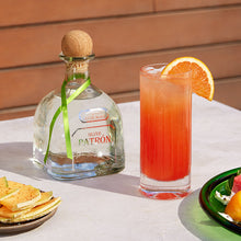 Load image into Gallery viewer, Patron tequila bottle with a cocktail and snacks on a table