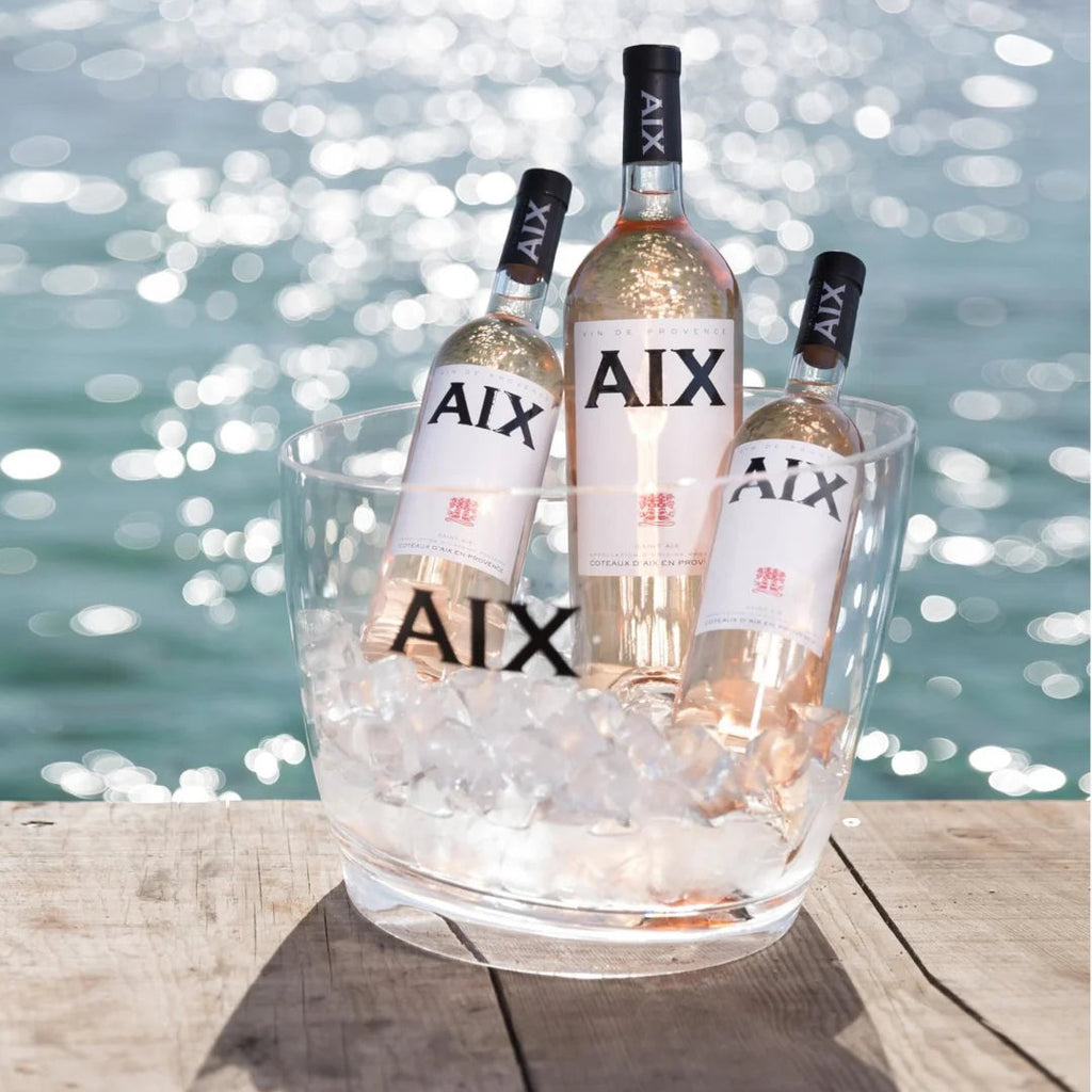 Three bottles of AIX wine in a glass ice bucket by a waterfront.