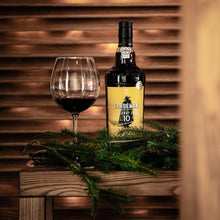 Load image into Gallery viewer, Sandeman Port wine bottle with a glass on a wooden surface with a wooden background
