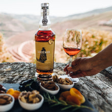 Load image into Gallery viewer, Bottle of Sandeman Port with a glass of port wine on a stone surface with scenic background