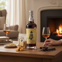 Load image into Gallery viewer, Bottle of Sandeman 20-year-old Port on a table with glasses and snacks in a cozy room.