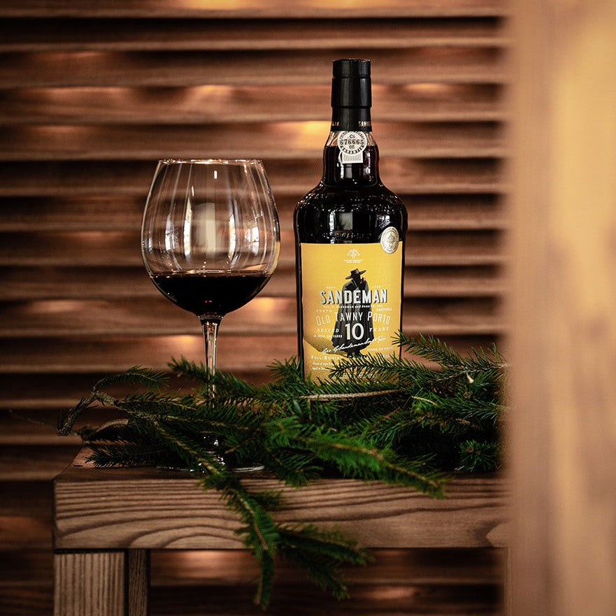 Sandeman Port wine bottle with a glass on a wooden surface with a wooden background
