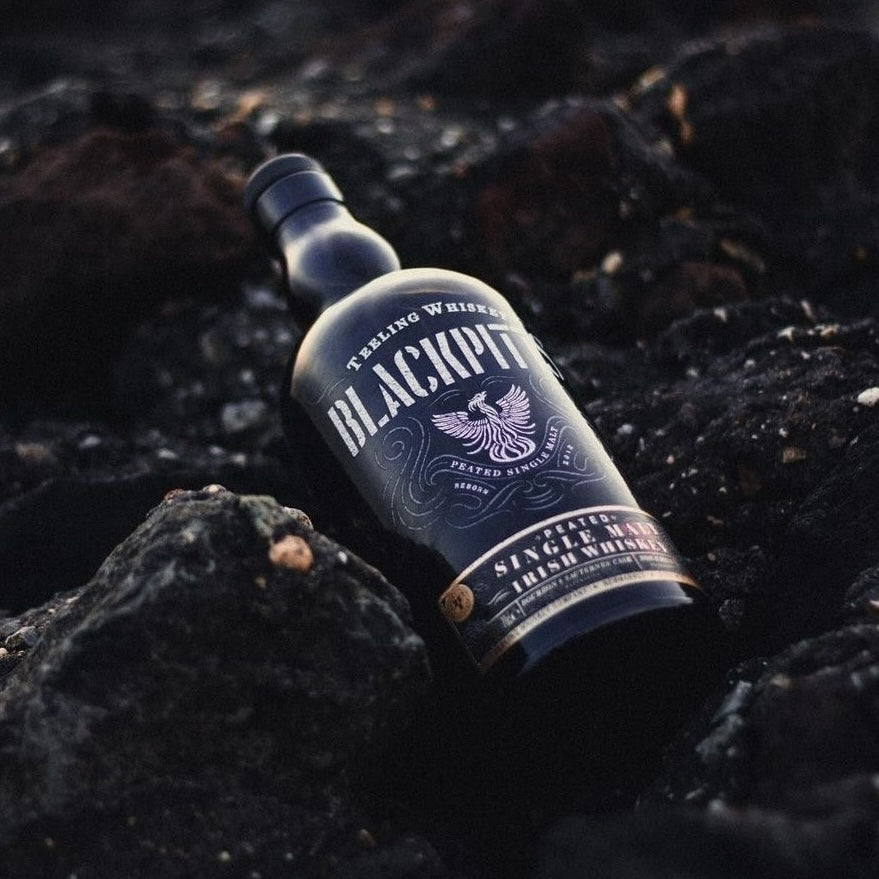 Load image into Gallery viewer, A bottle of Teeling Irish whiskey laying on black rocks