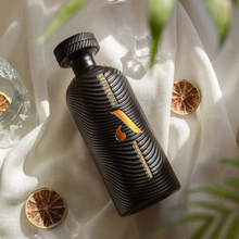 Load image into Gallery viewer, Black bottle of Artisan dry gin with orange label on a white fabric background with dried oranges and leaves.