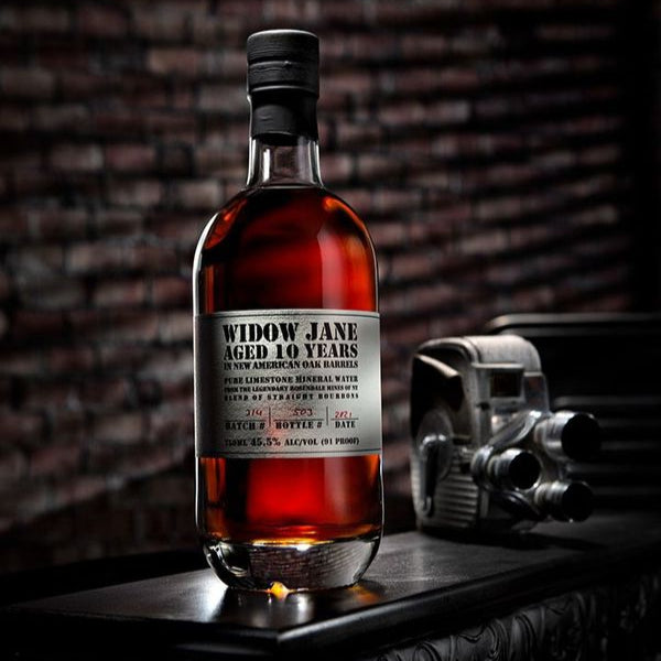 Bottle of Widow Jane aged 10 years whiskey on a wooden surface with a brick wall background.