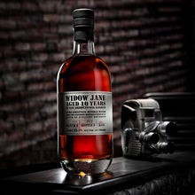 Load image into Gallery viewer, Bottle of Widow Jane aged 10 years whiskey on a wooden surface with a brick wall background.