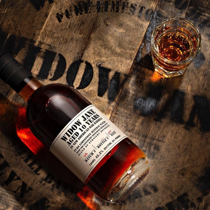 Load image into Gallery viewer, A bottle of Widow Jane 10YO Straight Bourbon laying down on a wooden barrel 