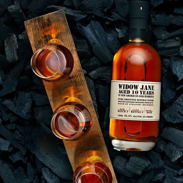Widow Jane 10 Years old whiskey bottle with three glasses on a bed of coal.